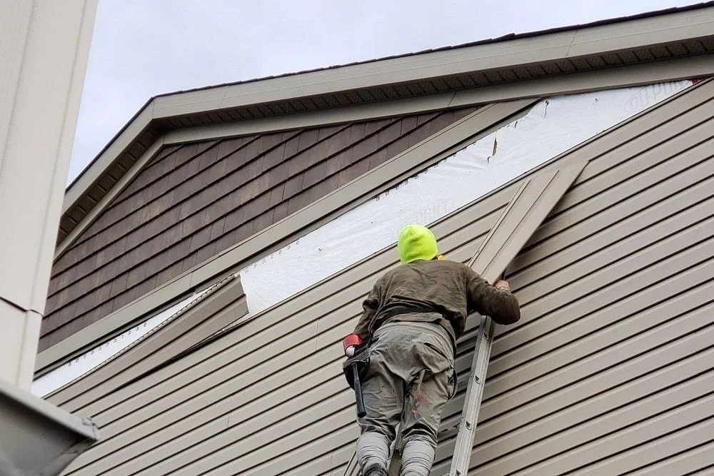 Contractor on a ladder installing new exterior vinyl and shake siding on a home in San Antonio, TX, handled by JD Local Builders.